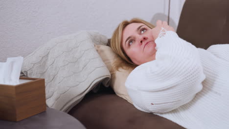 close up of participant lying on sofa during therapy session reaching for tissue on table to wipe nose, emotional moment captured with knit sweater and soft pillows in warm indoor setting