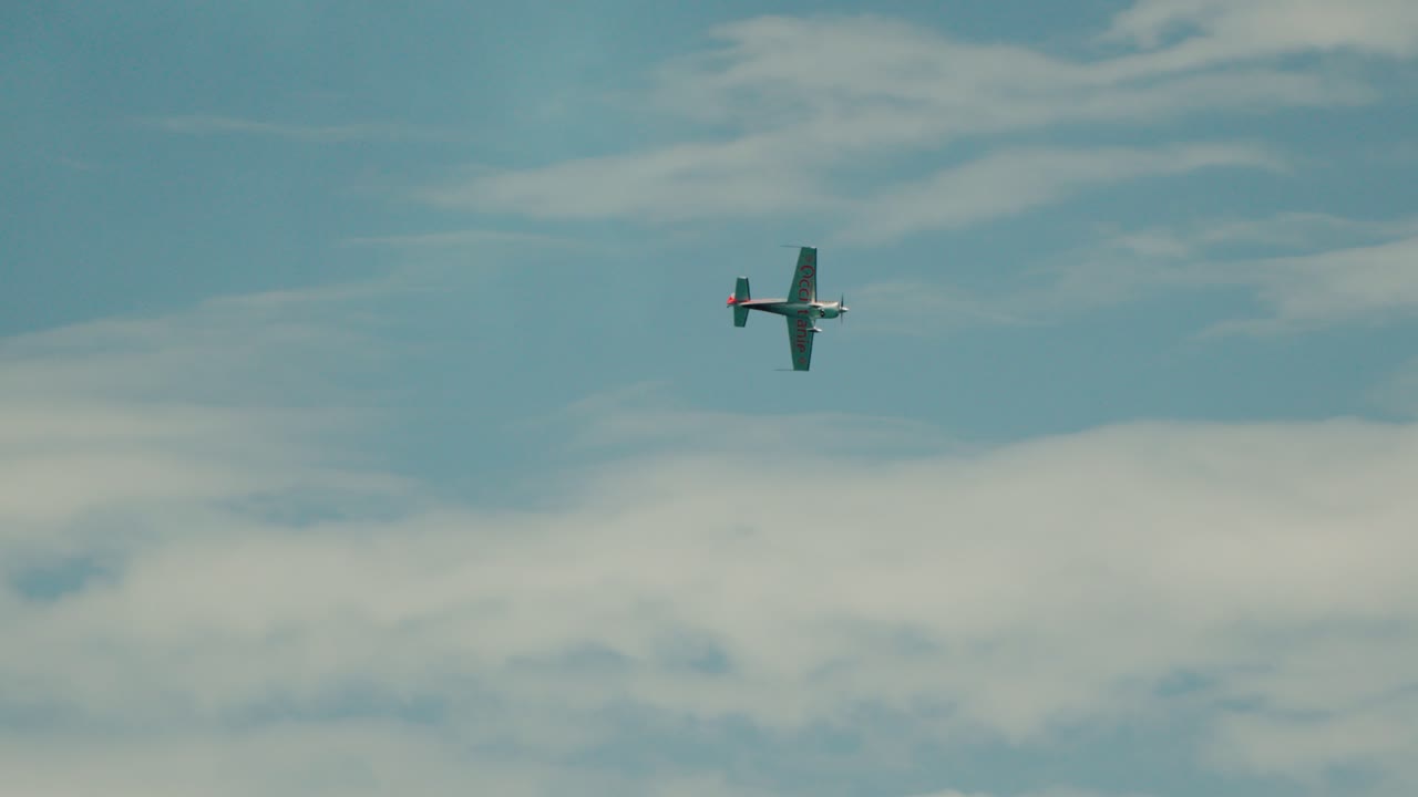 A small aircraft is flying through the blue sky with clouds