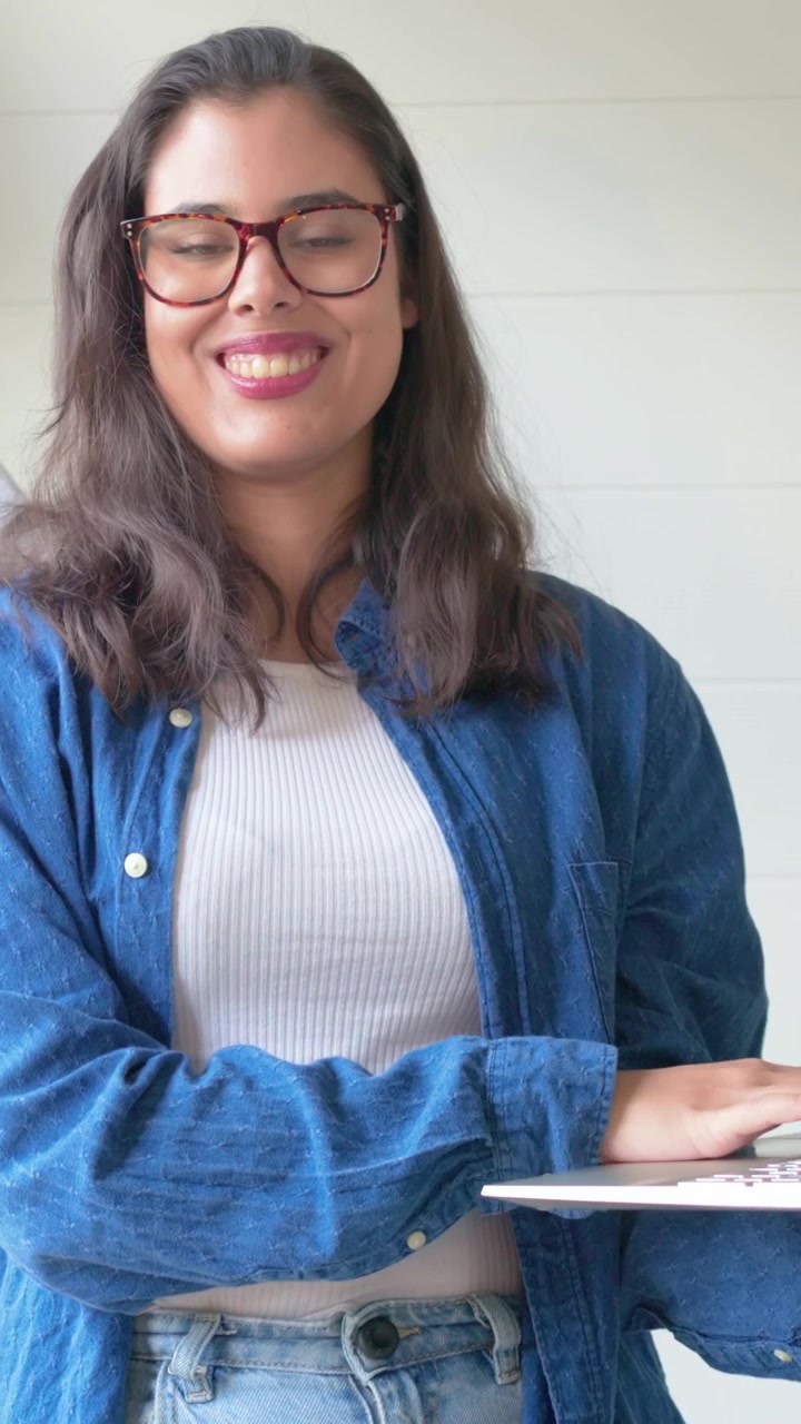 Mujer con gafas y camisa vaquera, comenzando a escribir en un portátil en una mesa estrecha, haciendo una demostración.