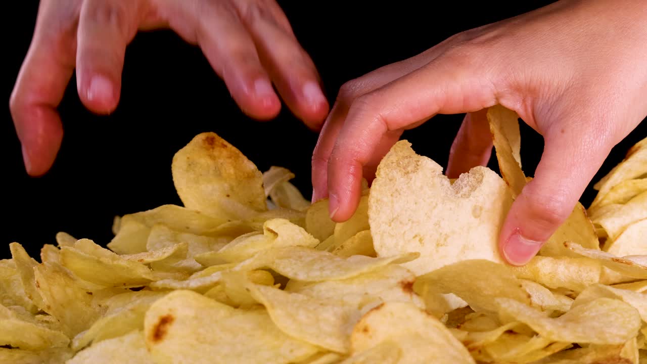 Mano umana che raggiunge una pila di patatine, illuminazione drammatica, primo piano, sfondo nero