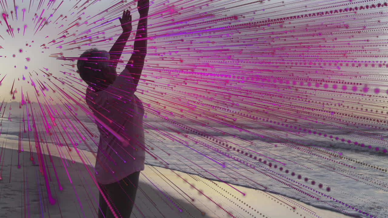 Senior woman raising arms on seaside boardwalk at sunset, showing tech digital streaks and pixels