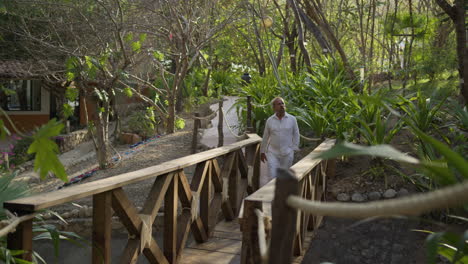 An-older-adult-walks-peacefully-on-a-wooden-bridge-while-admiring-the-surrounding-nature