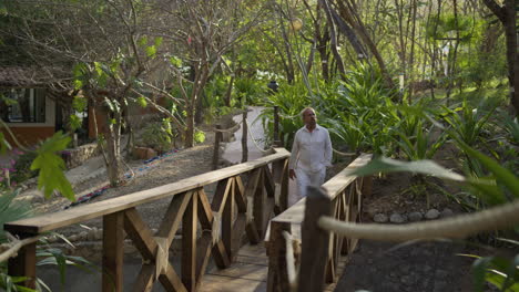 un adulto mayor camina tranquilamente sobre un puente de madera mientras admira la naturaleza que lo rodea