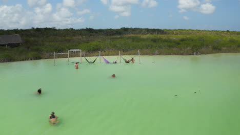 Slide-and-pan-footage-of-people-enjoying-hot-day-in-water.-Pastel-green-colour-in-natural-lake-in-tropical-destination.-Kaan-Luum-lagoon,-Tulum,-Yucatan,-Mexico