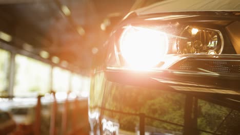 Car-headlight-turning-on-in-a-dimly-lit-garage-with-a-sunlit-background,-featuring-a-panning-shot