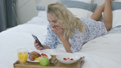 mujer usando un teléfono inteligente durante el desayuno en la cama