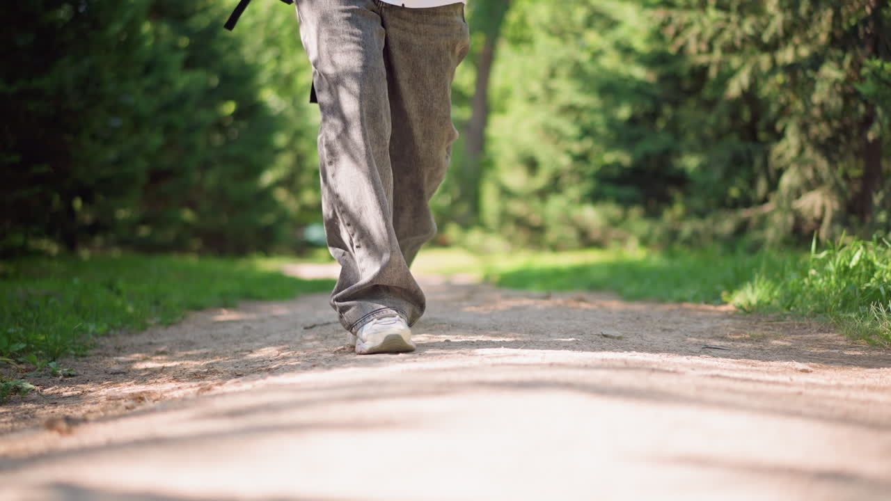 low angle feet on sunlit path, hiker or walker moving at steady leisure pace, backpack hint, soft tree canopy, relaxed jeans, healthy outdoor therapy, morning calm, mindful breathing