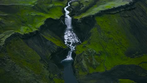 aerial drone footage of a gorgeous and beautiful waterfall in the mountain landscape of greenland or iceland during a cloudy weather day. waterfall is falling off a cliff that has moss, sharp edges.