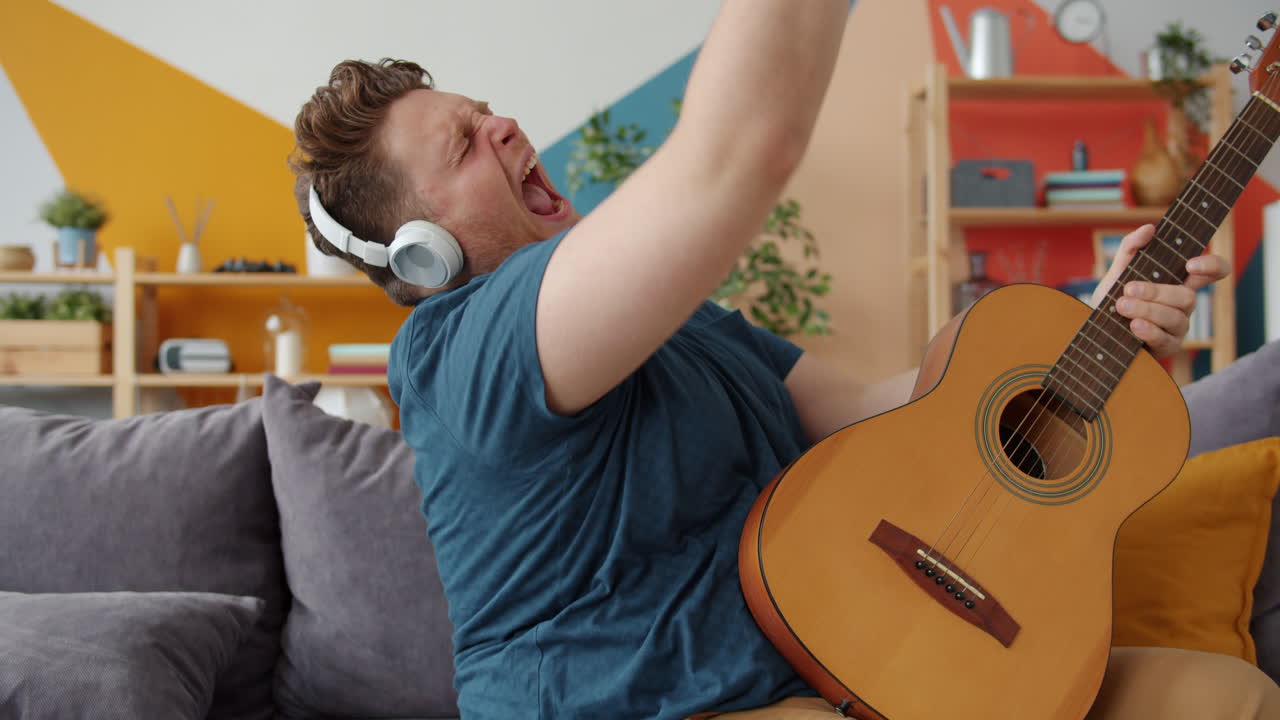 Man Singing Along to Music While Playing Guitar on a Couch