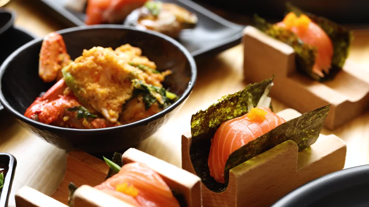 Camera pans over assorted Asian dishes: fried rice, tempura, dipping sauces, and salmon sushi
