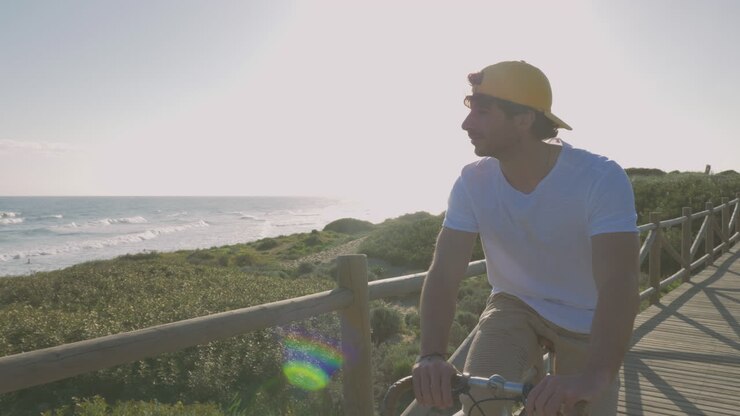Ciclista masculino em um calçadão em direção à praia olhando para o mar