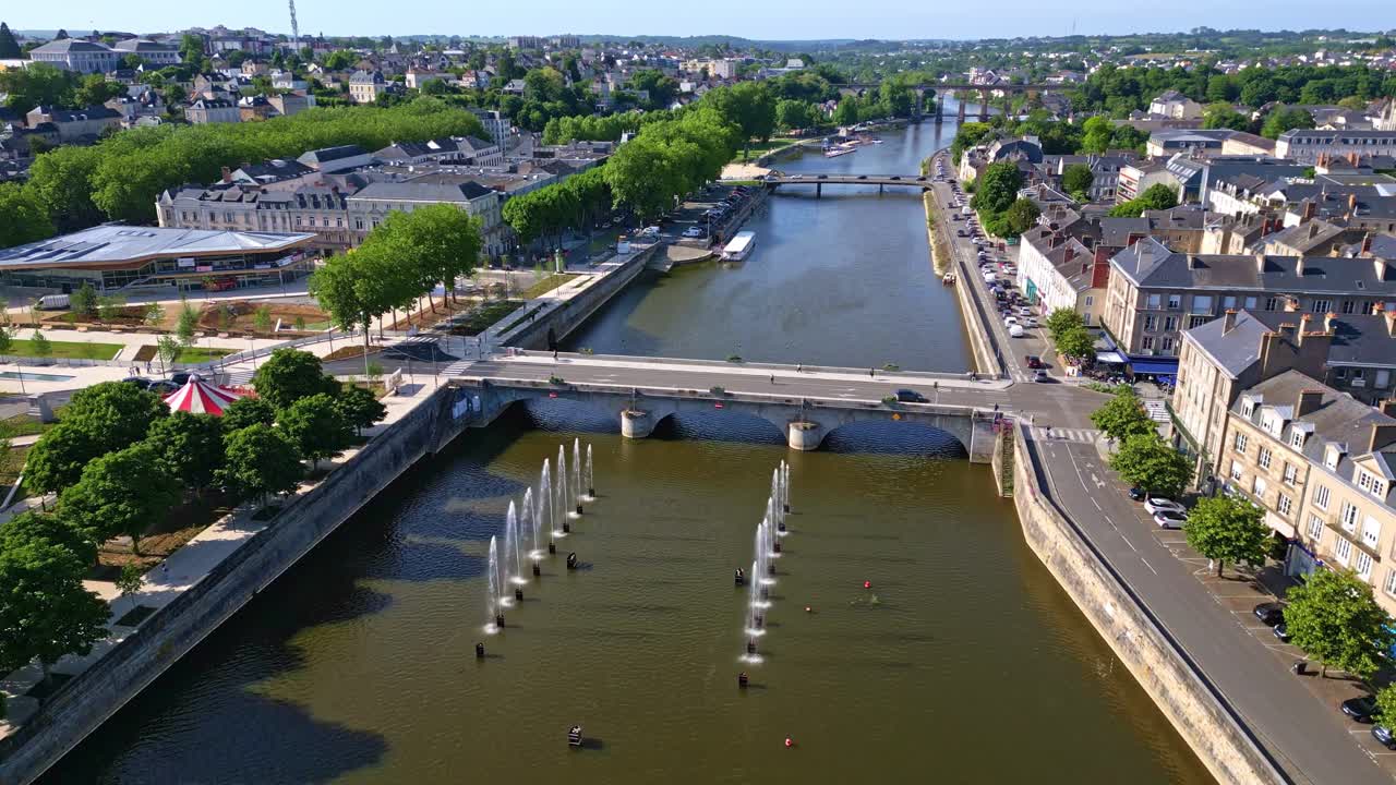 Lateral drone shot pivoting above Mayenne River, showing fountains, Place du 11 Novembre, bridge, and cityscape. France