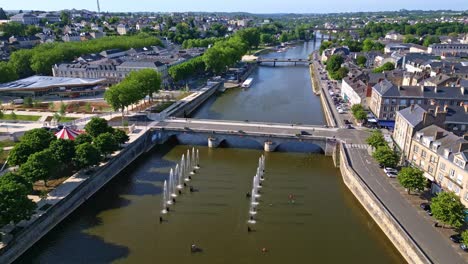 lateral drone shot pivoting above mayenne river, showing fountains, place du 11 novembre, bridge, and cityscape. france