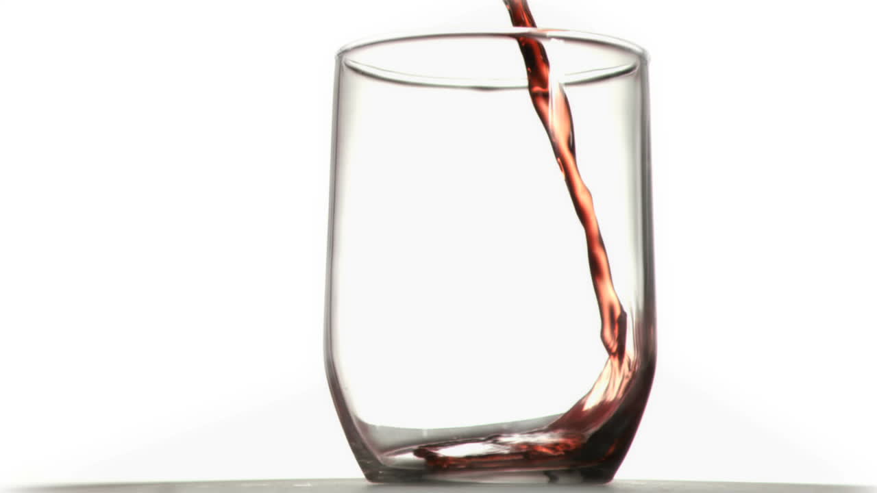 Red thin trickle in a super slow motion falling in a glass 