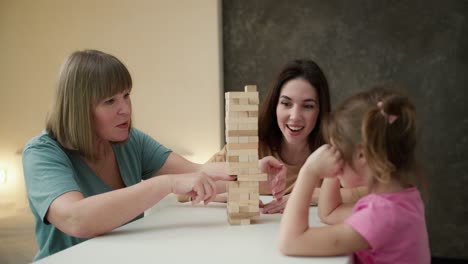 Glückliches-Kleines-Mädchen-Mit-Mutter-Und-Großmutter,-Die-Drinnen-Zu-Hause-Jengo-Spielen