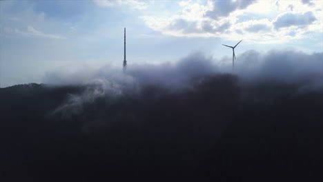 toma aérea de una gran torre de radiodifusión y un generador de viento atravesando la capa de nubes sobre la montaña del bosque negro hornisgrinde en un día soleado por la mañana