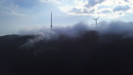 aerial shot of big broadcasting tower and wind generator stinging through the cloud cover over the black forest mountain hornisgrinde on a sunny day in the morning