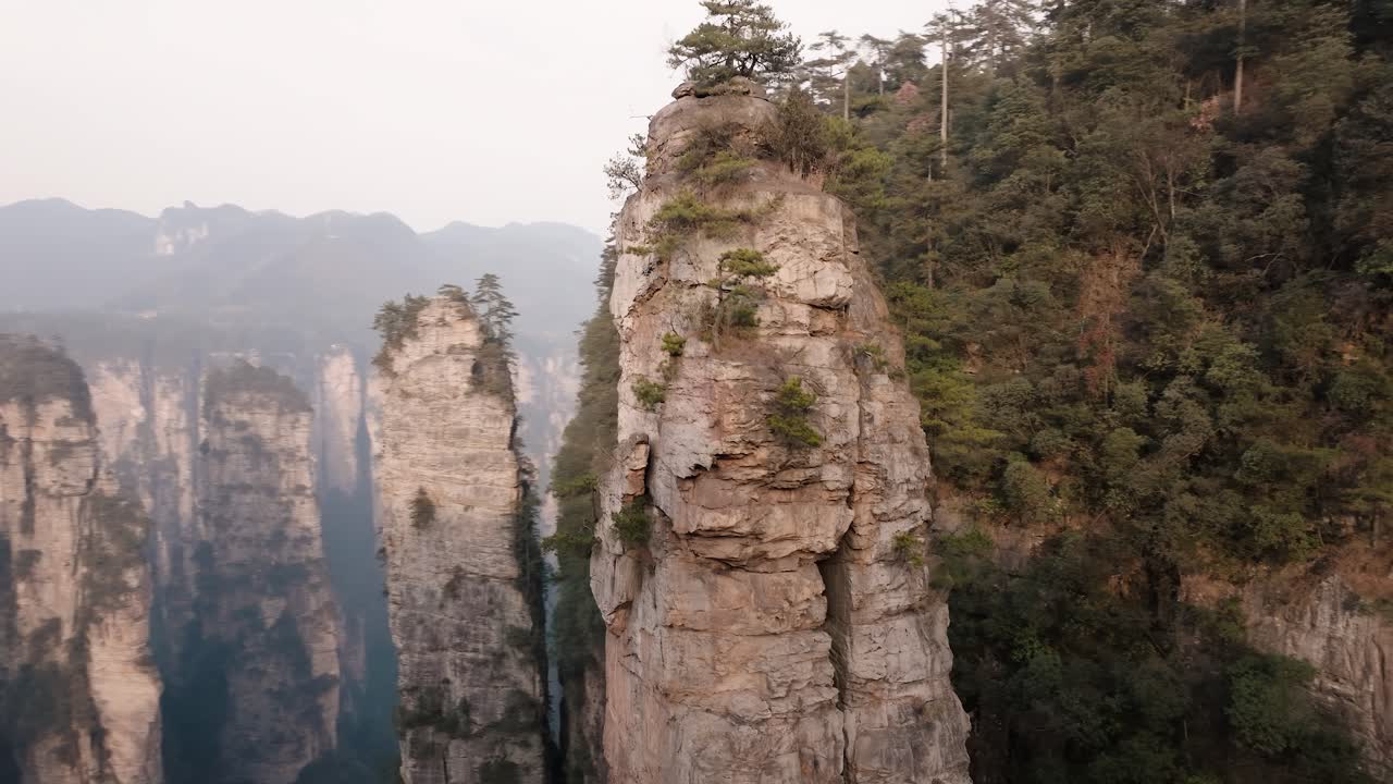 Close aerial view of a towering sandstone pinnacle with sparse trees growing on top, surrounded by cliffs in Zhangjiajie National Park