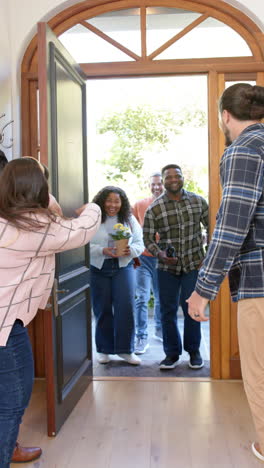 vertical video of happy diverse couple welcoming friends in sunny house