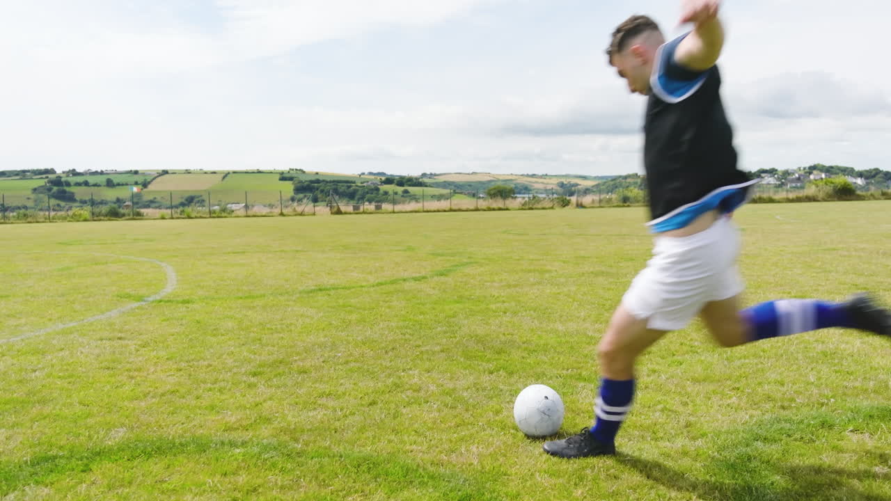 Male soccer players practicing kicking balls and wearing black and yellow vests on pitch, copy space