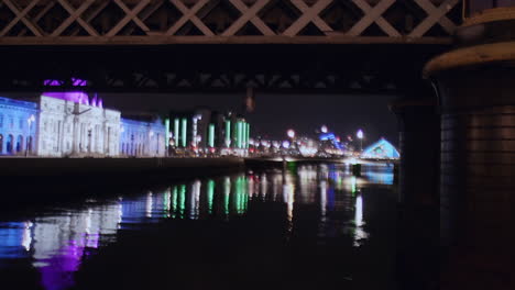 dublin nightlife during christmas: custom house and samuel beckett bridge shine, framed under loop line bridge