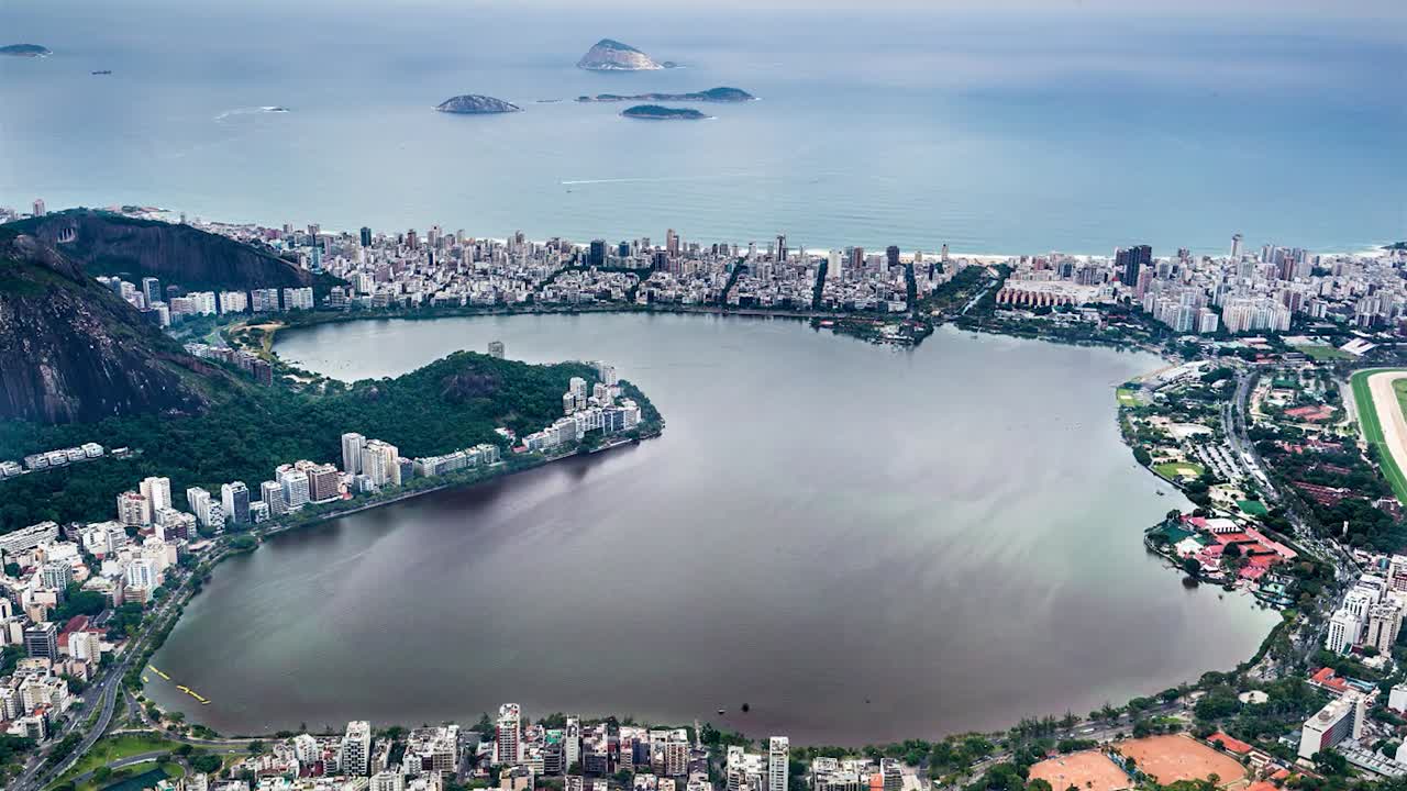 Filmagem em time-lapse da Lagoa Rodrigo de Freitas no Rio de Janeiro, Brasil. A forma distinta de rim da lagoa é cercada por áreas urbanas densamente povoadas, edifícios residenciais e espaços verdes.