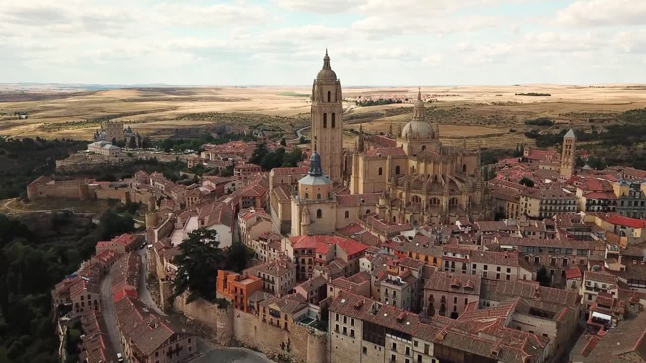 A breathtaking aerial view of Segovia, Spain, highlighting its historic cathedral, ancient walls, and charming medieval architecture surrounded by expansive landscapes under a bright sky
