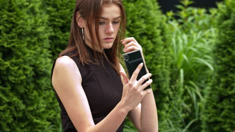 girl in black dress fixing her hair using smartphone as a mirror