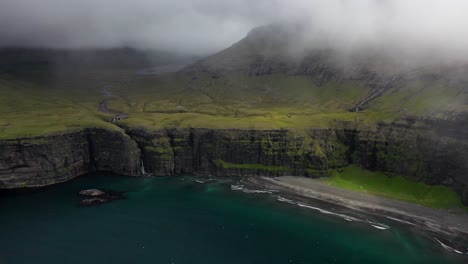 faroe islands coastline through thick sea mist and clouds, aerial view pull back