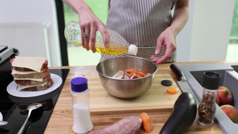 person pouring oil into a bowl of vegetables for cooking