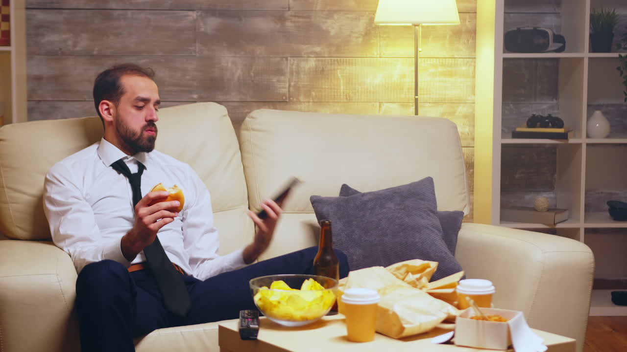 Businessman with tie sitting on couch eating a burger