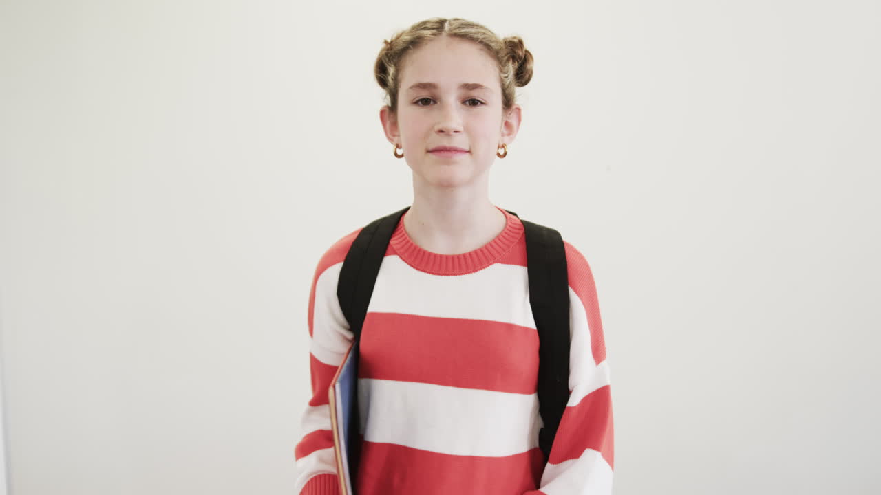 Smiling young girl with backpack holding books, ready for school day, copy space