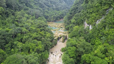 Drone-aerial-footage-of-Semuc-Champey-National-Park-surrounded-by-bright-green-rainforest-hillsides-and-mountains