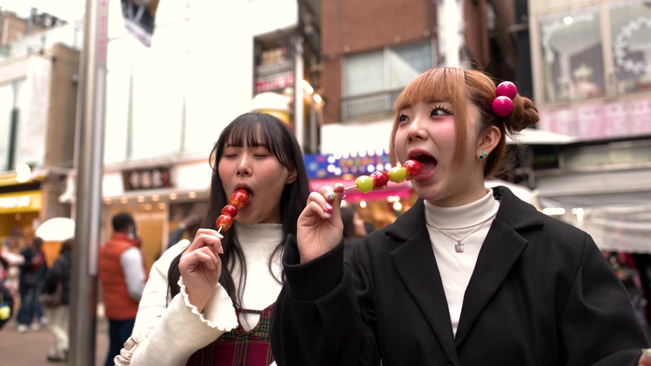 Due giovani donne asiatiche che mangiano frutta candita per strada in città