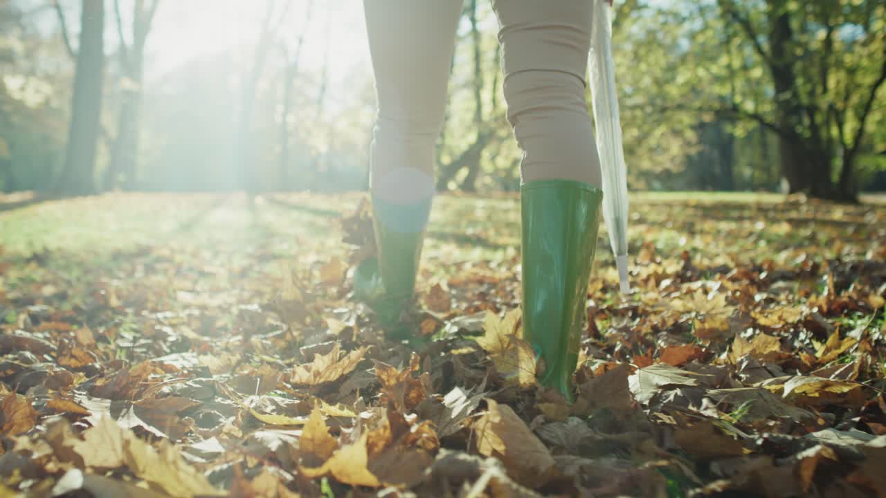 Low section of woman's legs wearing rain boots walking in forest with umbrella.