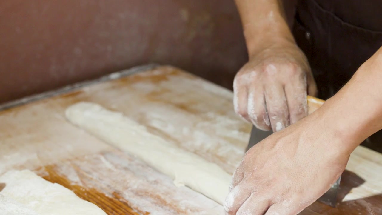 Close-up of chef using metal scraper and rolling pin on flour-covered wooden surface.