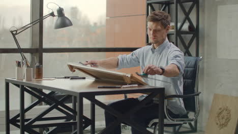 architect man standing working with blueprints sketching a construction project on wood desk at home office.construction design concept.vintage color tone. engineer works in a bright office with a large window concentrates and draws blueprints. workplace of an architect or designer: loft style minim