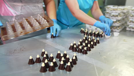 confectionery worker extracts candies from molds. other worker puts ready-made sweets into a packaging paper. close up.