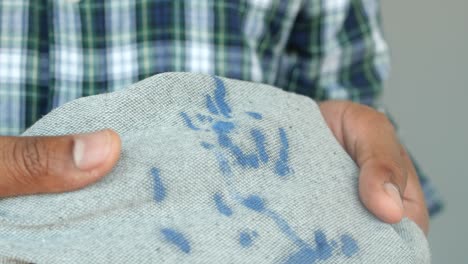 close up of a man's hands holding a grey cloth with blue paint splatters.