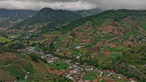 Cerro-Punta-Panama-Aerial-v3-birds-eye-view-overlooking-at-foothill-town-surrounded-by-cultivated-farmland,-tilt-up-reveals-mountainscape-with-dense-stormy-clouds---Shot-with-Mavic-3-Cine---April-2022