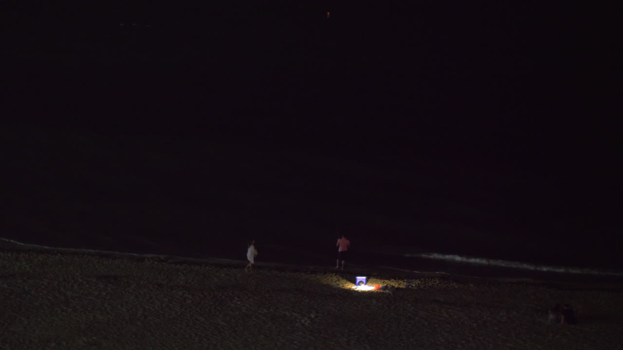 vista nocturna de personas relajándose en la playa y mirando el mar oscuro