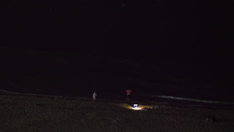 vista nocturna de personas relajándose en la playa y mirando el mar oscuro