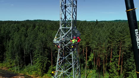 Pylon-Workers-Wearing-Safety-Harness-And-Hard-Hats-Working-On-The-Assembly-Of-High-Voltage-Electrical-Tower-On-A-Sunny-Day