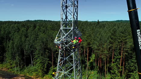 pylon workers wearing safety harness and hard hats working on the assembly of high voltage electrical tower on a sunny day