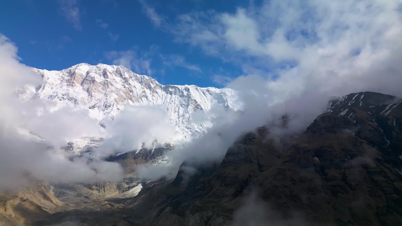 Majestic Dhaulagiri Range in Nepal with snow-covered peaks rising above drifting clouds under a clear blue sky, capturing the grandeur and serenity of the Himalayan mountainscape