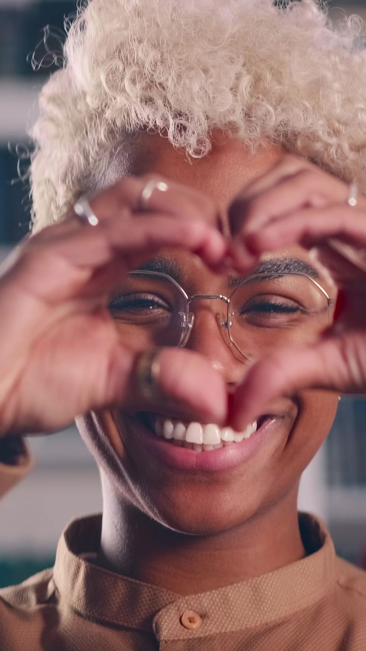 Donna afroamericana sorridente che fa un gesto a forma di cuore con le mani sugli occhi