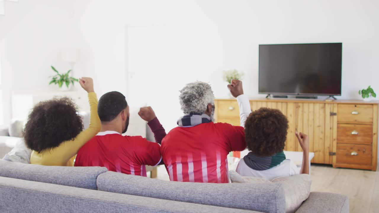 vista trasera de una familia de varias generaciones animando mientras ven deportes en la televisión en casa