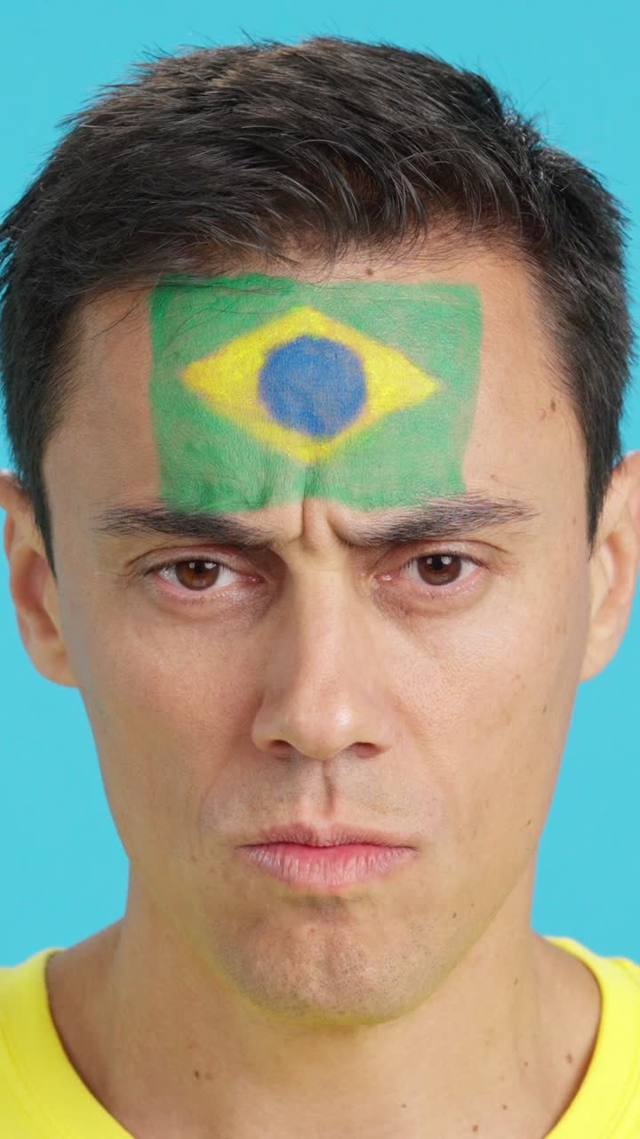 Hombre serio con una bandera brasileña pintada en la cara