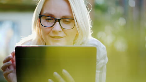 a young woman in glasses lies on a lawn in the park enjoys a tablet technology in nature 4k video