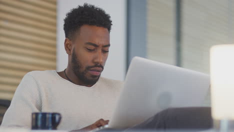 young businessman working late sitting at desk with laptop in modern open plan office
